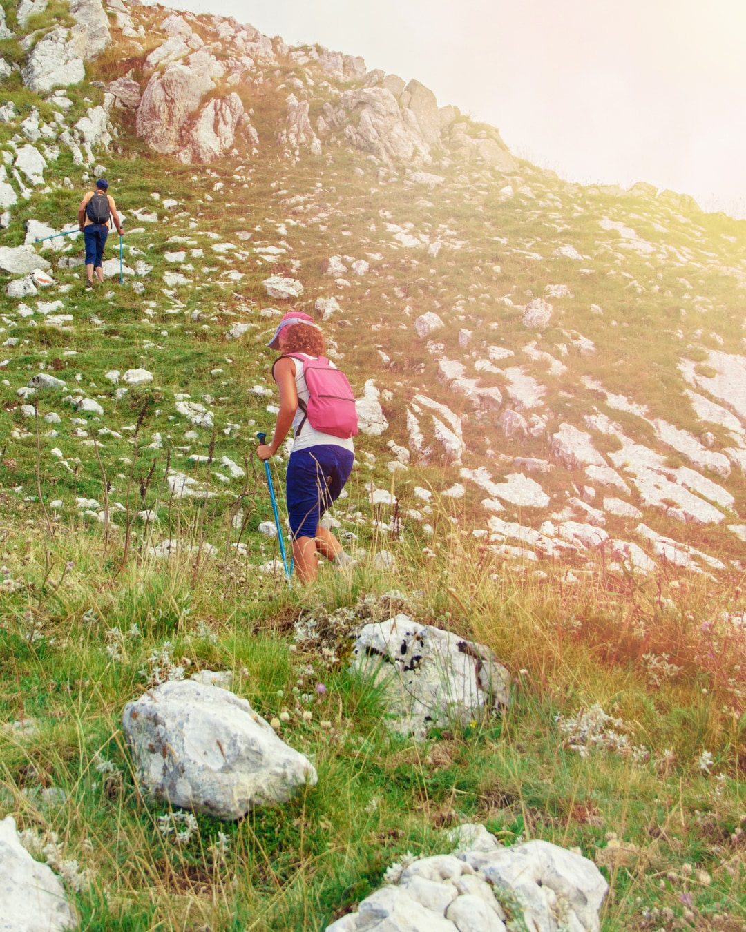 A couple hiking up a grassy mountain trail.
