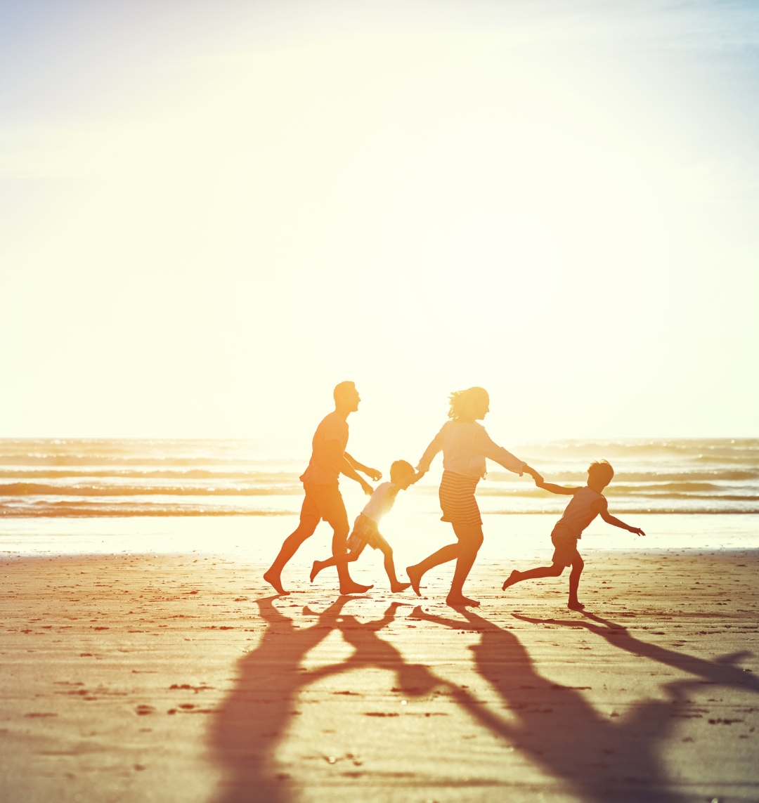 Silouette of a family with young children running on the beach.
