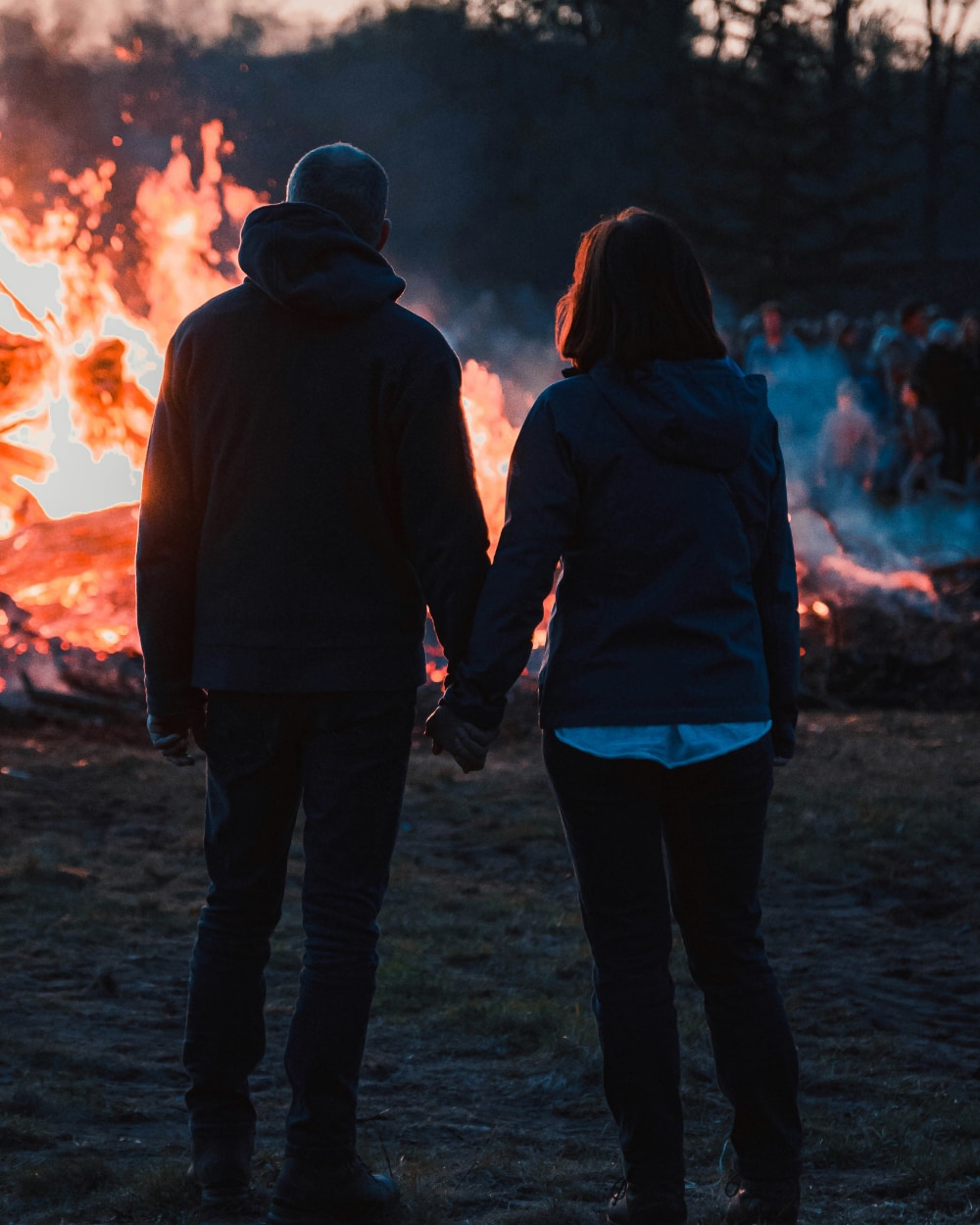 A man and woman hold hands while watching a bonfire.